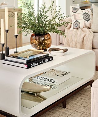 A white coffee table with two tiers and an assortment of accessories on top