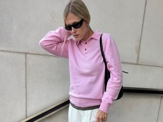 Woman wears a pink polo sweater, white baggy trousers, boat shoes and wraparound sunglasses.