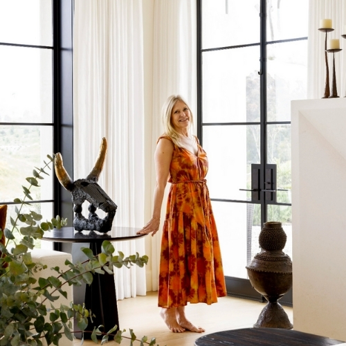 Image of a woman in an orange-red dress standing in a large, luxurious white room with floor-to-ceiling windows.