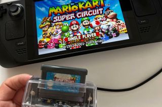 GameBoy cartridge peripheral in foreground with cord connecting it to Steam Deck displaying Mario Kart: Super Circuit splash screen