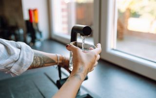 hand holding glass being filled with water from black kitchen tap over kitchen sink