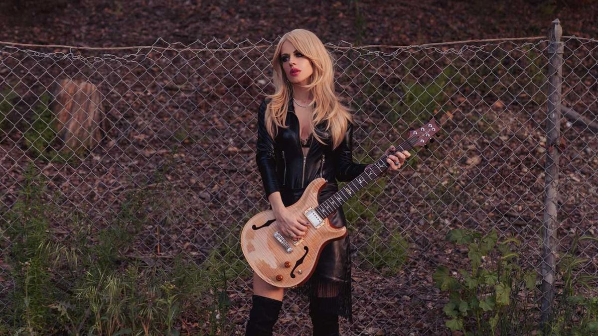 Orianthi playing guitar in front of a wire fence