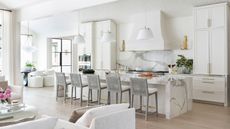 A white kitchen with marble counters and a layered lighting scheme