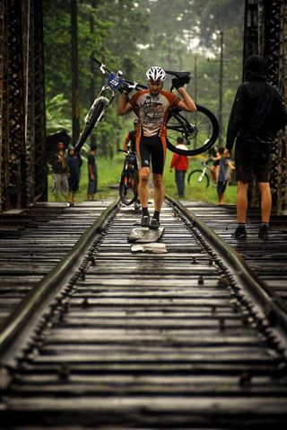 A rider carries his bike across the railroad tracks.