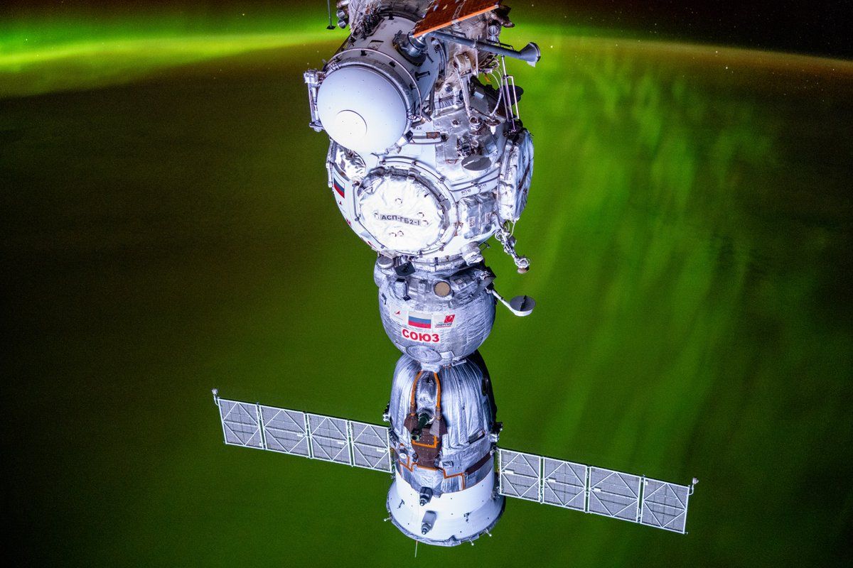 a spacecraft with solar wings in front of a green aurora on earth