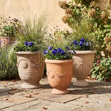 Urn planters from Amazon, Walmart and Anthropologie planted with ornamental grasses and pansies in a garden