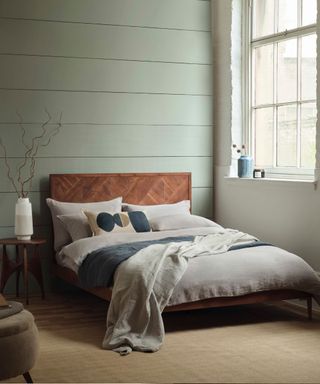 bedroom with soft blue panelled, a wooden bed and grey sheets