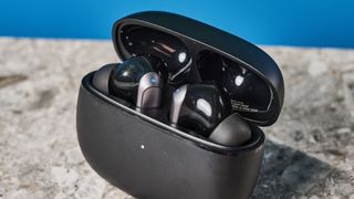 a pair of black and silver earbuds with silicone tips and a black charging case is photographed against a blue background