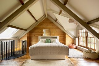 double bedroom in loft with natural wood cladding and dark wood floors and neutral bedlinen