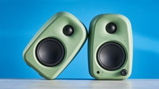 Kanto UKI bookshelf speakers in sage photographed in front of a blue background