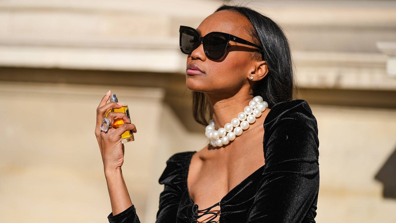 Emilie Joseph @in_fashionwetrust wears black sunglasses, diamond earrings, a white large pearls necklace, a black laces V-neck / shoulder-pad / long sleeves / short ruffled velvet dress, black tights, a large crystal ring, black shiny leather pointed pumps heels shoes, during a street style fashion photo session, on October 24, 2021 in Paris, France