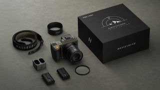 The complete Hasselblad X2D 100C Earth Explorer Edition camera kit, including lens, strap, batteries, charger, filter and hood, along with the limited edition packaging, on a textured grey surface