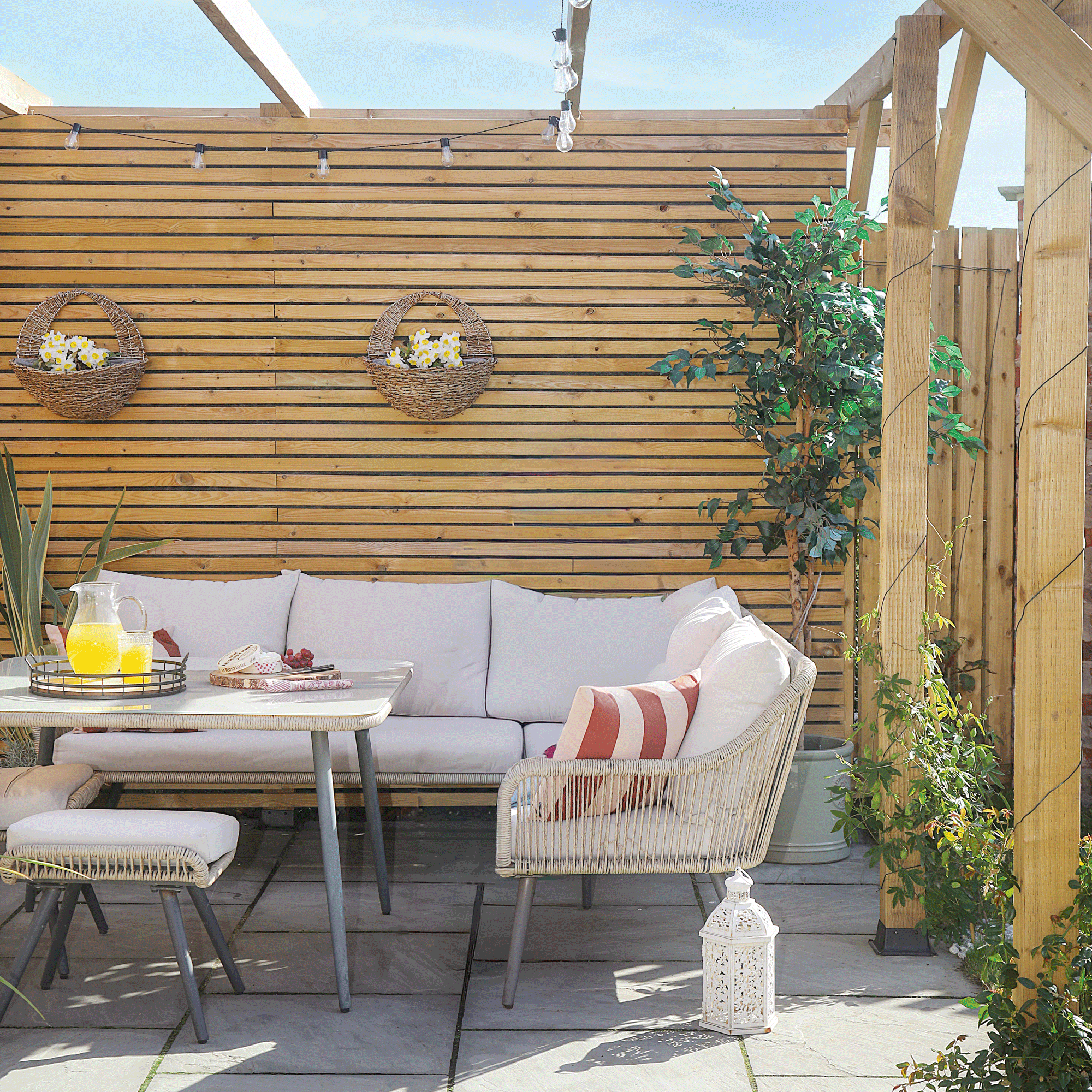 a patio area with a pergola and horizontal fencing with a corner outdoor sofa and hanging baskets