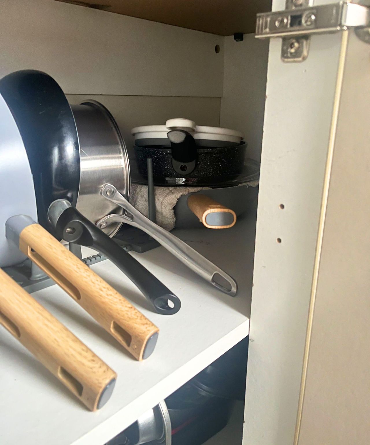 A grey peggy organizer being used in a white cabinet to organize pots and pans