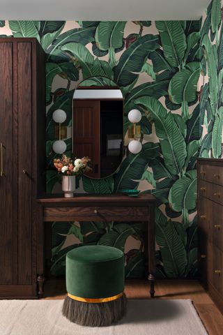 A corner in a bedroom with green stool and wallpaper, and dark brown wood cabient