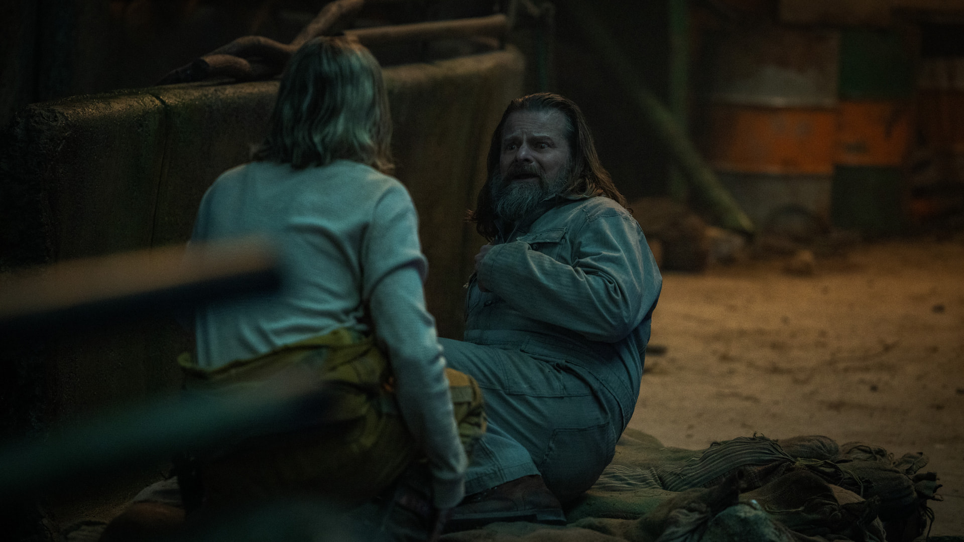 A woman tries to talk to a cowering man in a dark chamber