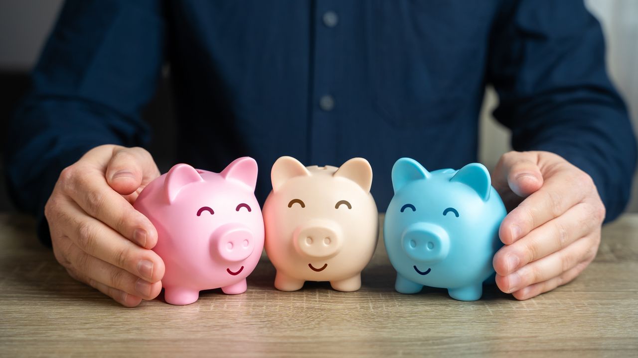 A man&#039;s hands flank three piggy banks in different colors.