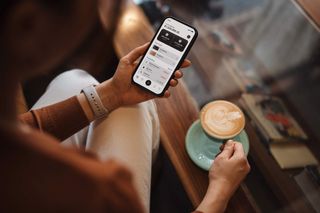 A person enjoying a coffee in a coffee shop while checking their budget on their mobile budgeting app. 