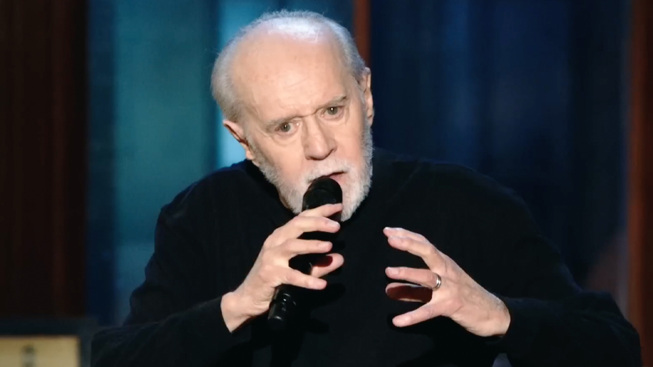 George dressed in black long sleeve shirt performing stand up featured in HBO's doc, George Carlin's American Dream.