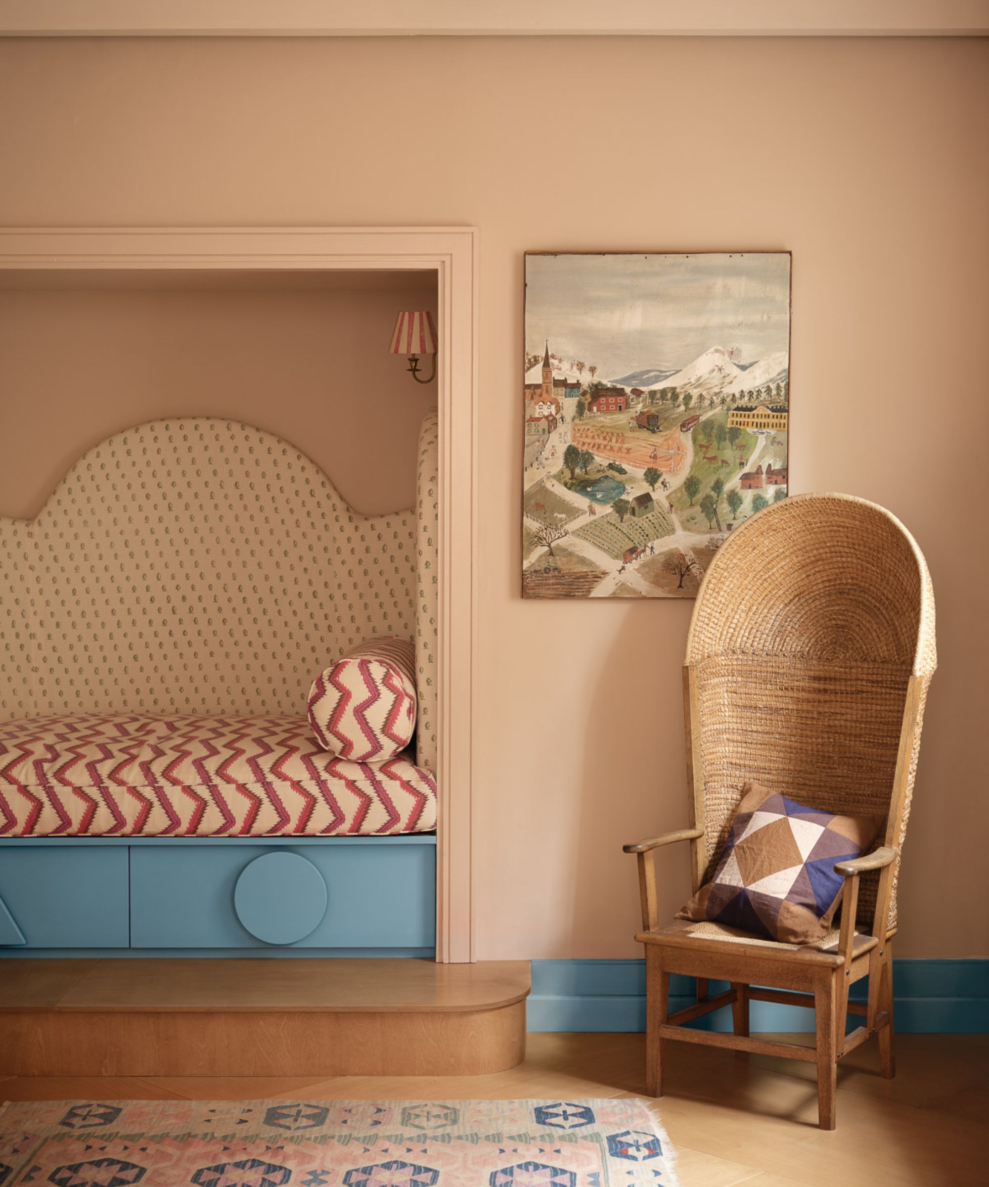 Quirky peach fuzz bedroom with bed alcove and wicker egg chair. There are mismatched patterns including zig zags on bed, dots on alcove headboard and geometric patterns on the egg chair cushion. The under bed storage and baseboards are a chalky blue