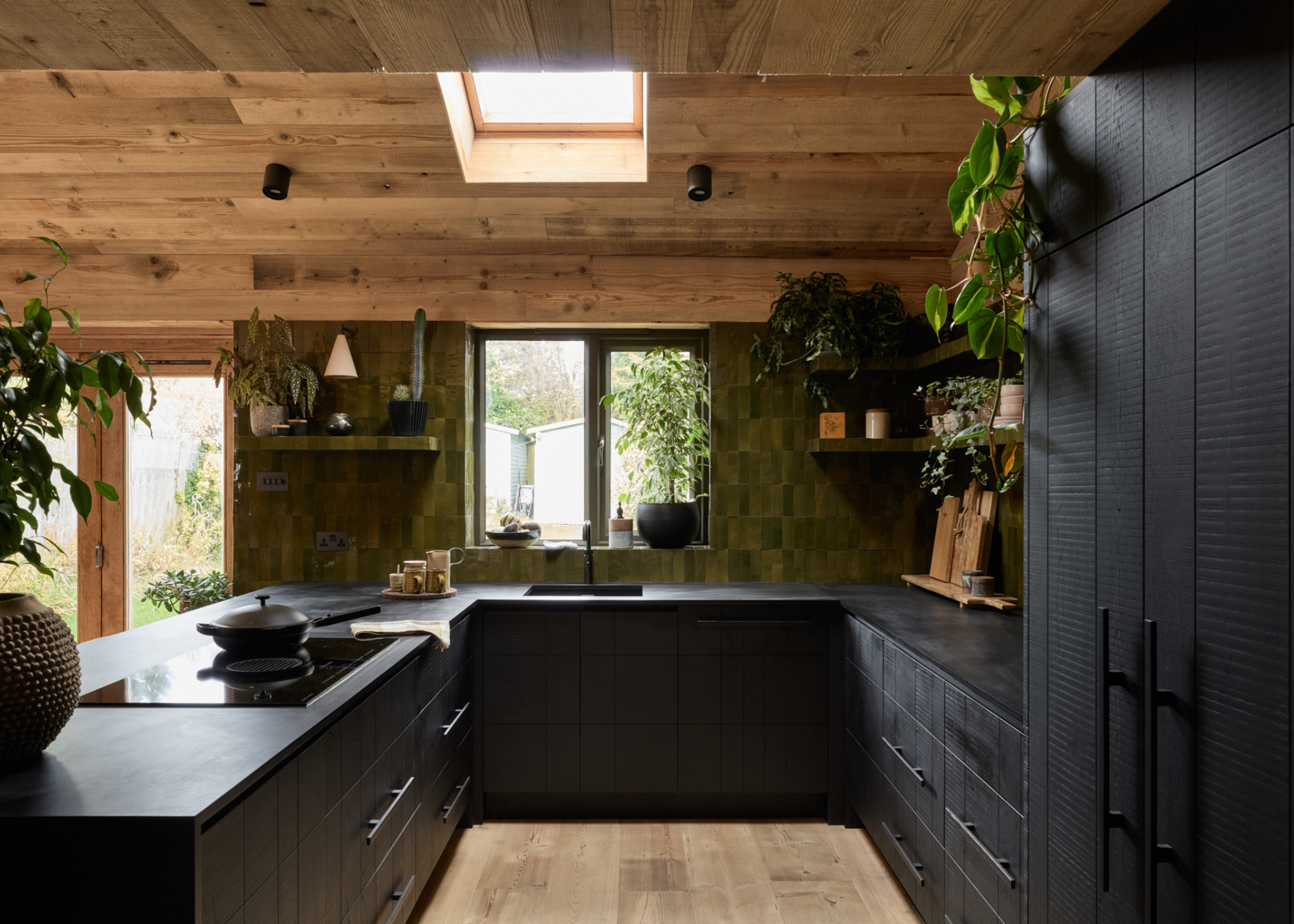 wooden clad kitchen with green zellige tiles on one wall and black wooden cabinetry across
