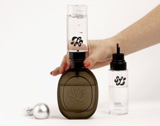 A woman filling a scent lab potion bottle with blendable mists in front of a plain backdrop