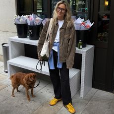 Lucy Williams in black-and-yellow Adidas sneakers, black pants, a white crewneck, and an oversized chore coat. 