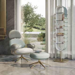 ‘Ensis’ armchair and foot rest in pale green and gray, combined with gold metal. The same colour scheme bookcase is next to it.