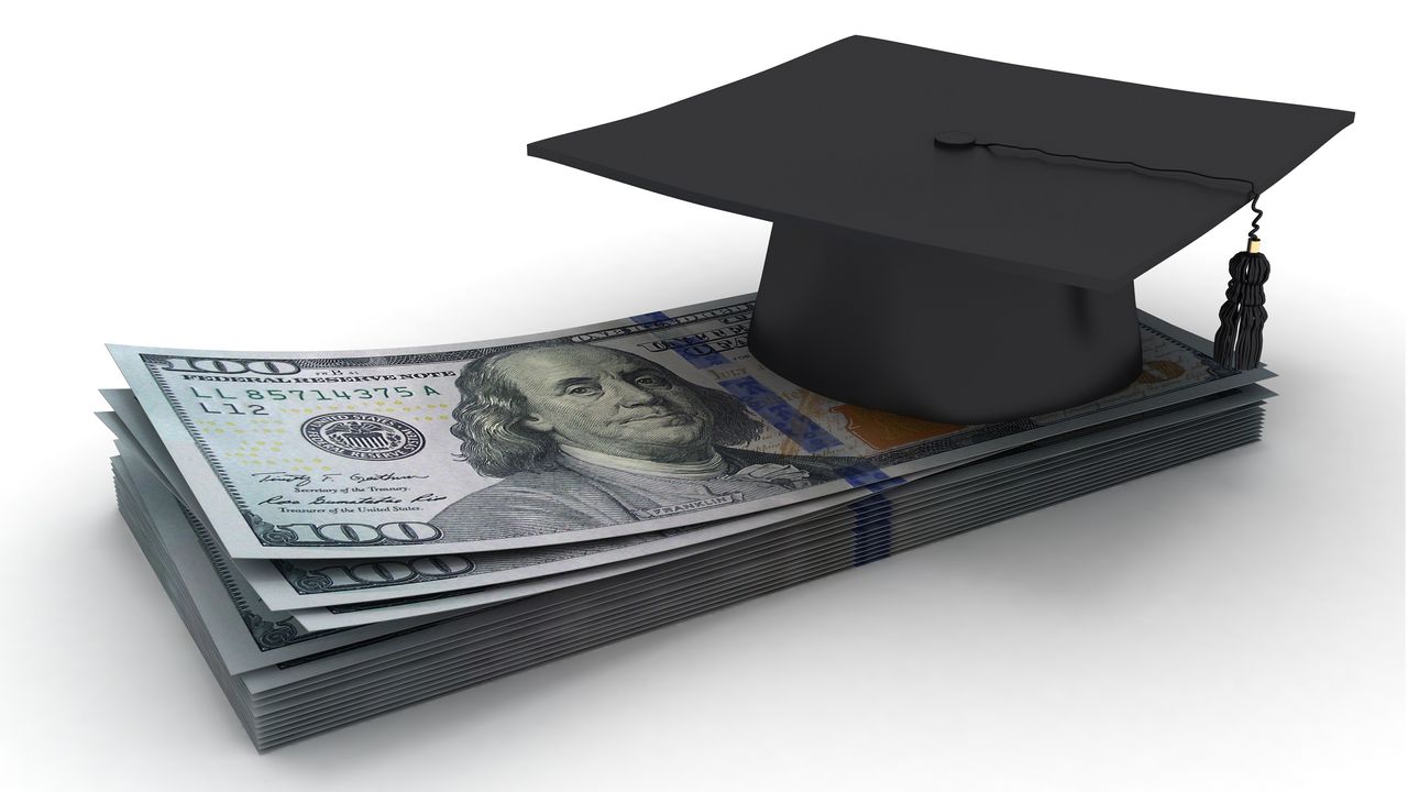 A mortar board sits atop a stack of hundred-dollar bills.