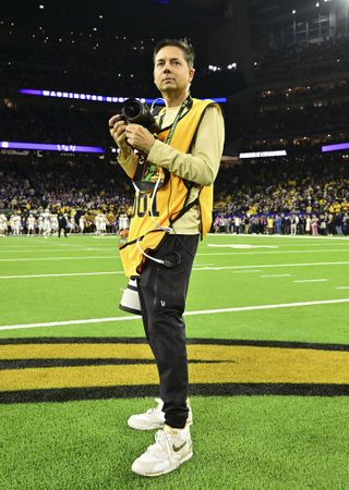 Sports photographer Kevin Jairaj stands in the middle of a football stadium holding his camera