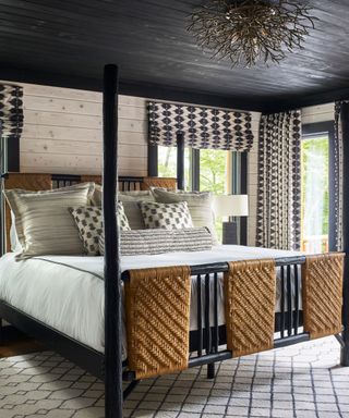 White sheets and gray pillows on a black and rattan bed base against a white wall and a black ceiling.