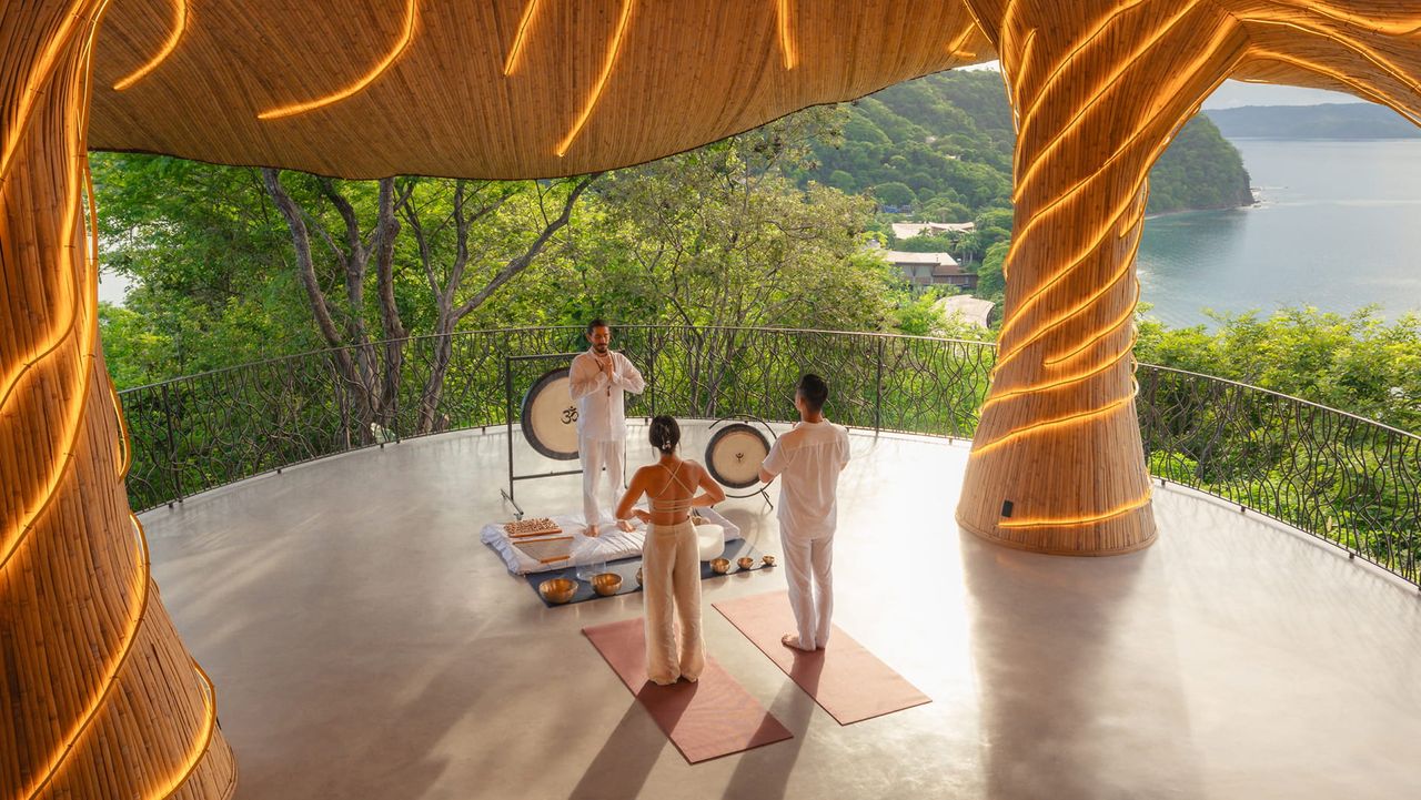 Image of three people doing yoga on a covered balcony high above the ocean.