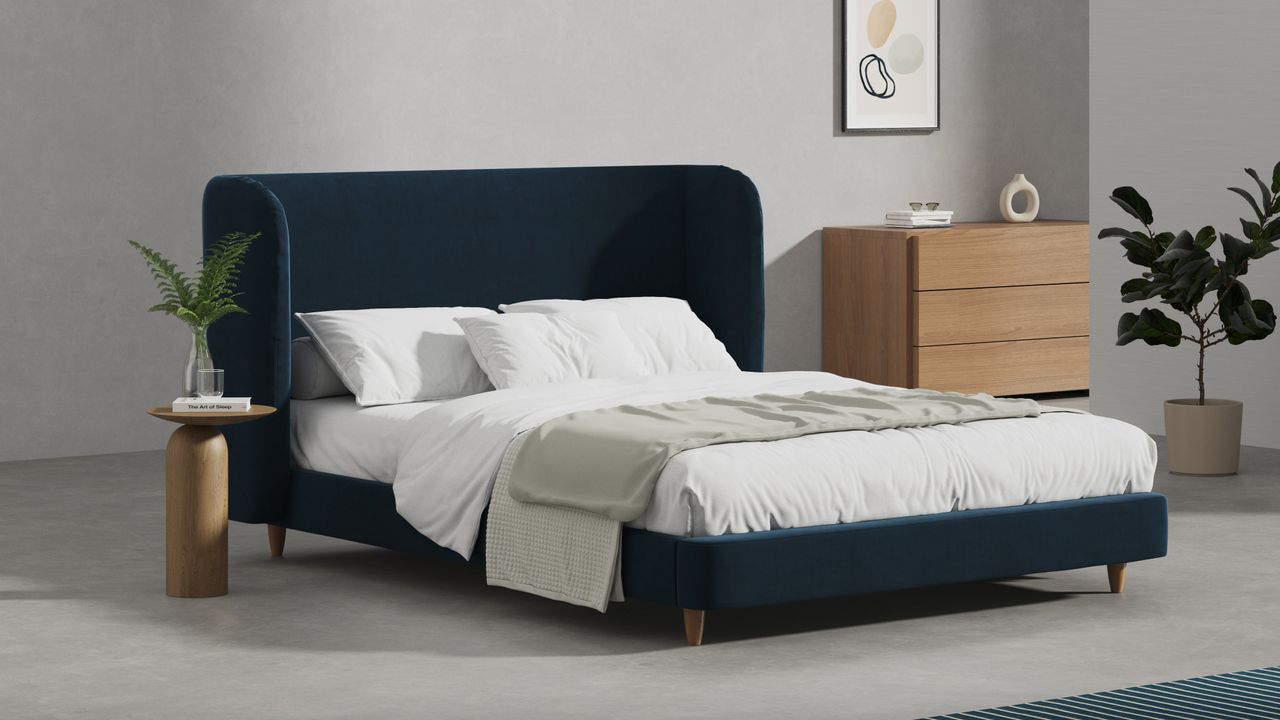 A blue upholstered bed frame with white bedding in a bedroom with a wooden chest of drawers