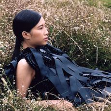 A model laying in long grass wearing a Ssense dress