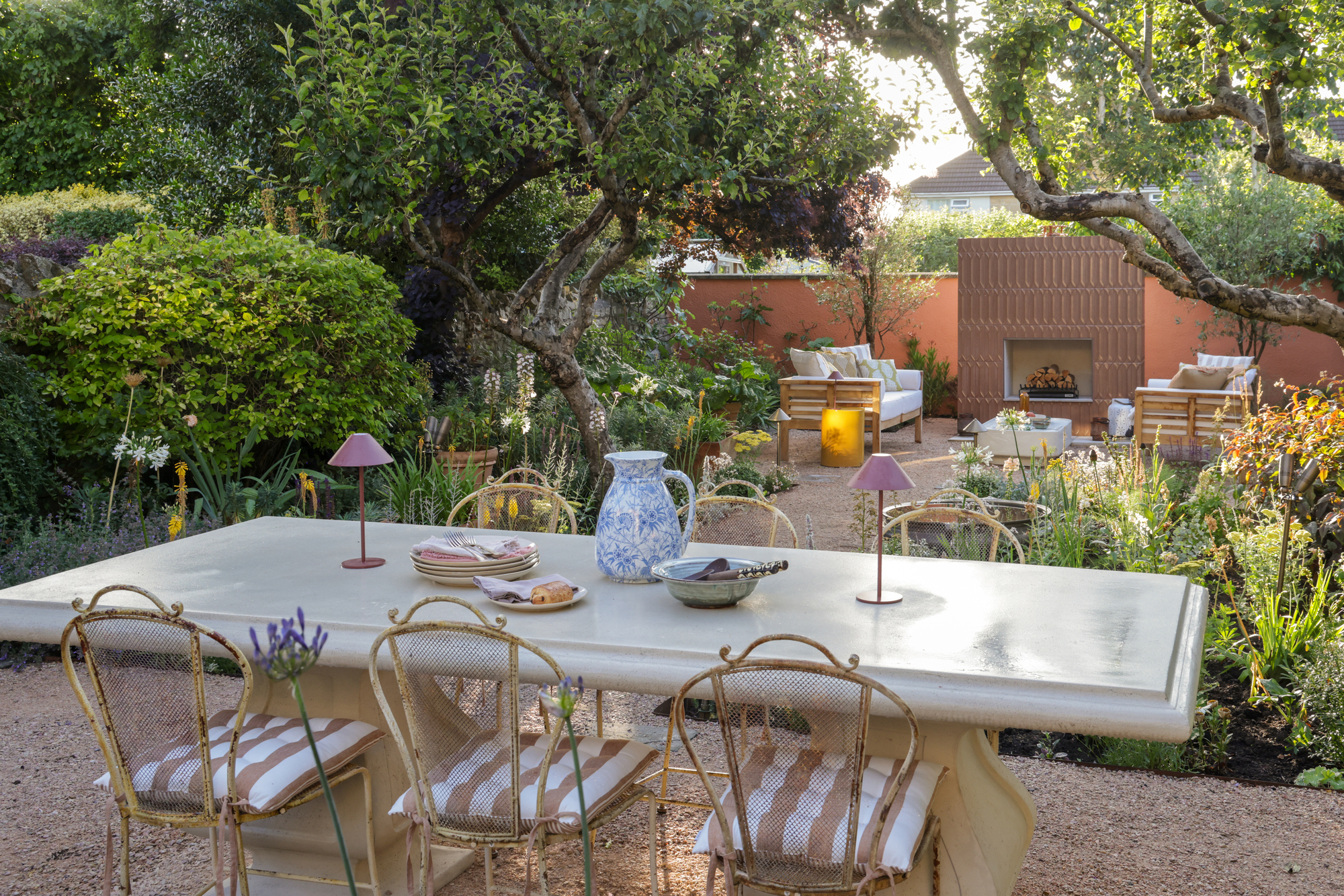 A garden with an outdoor dining table, garden borders, and an outdoor fireplace in the background
