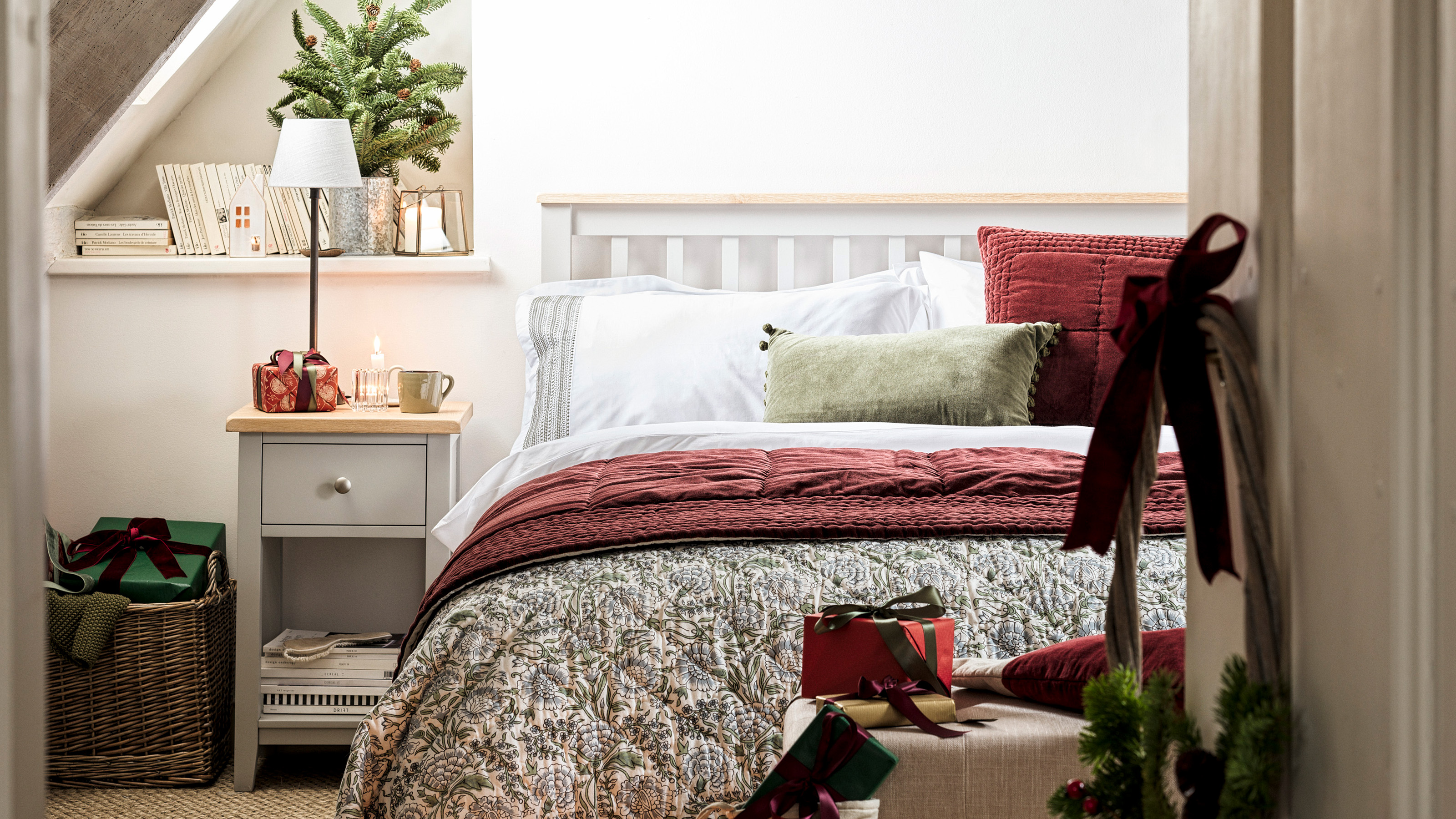 guest bedroom dressed for christmas with double bed with grey frame and matching bedside table with lamp white bedlinen and a green and red throw