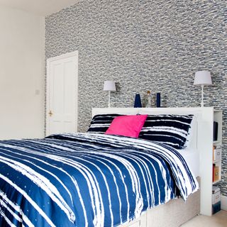 bedroom with bed blue designed bedding designed wallpaper white lamp and white door