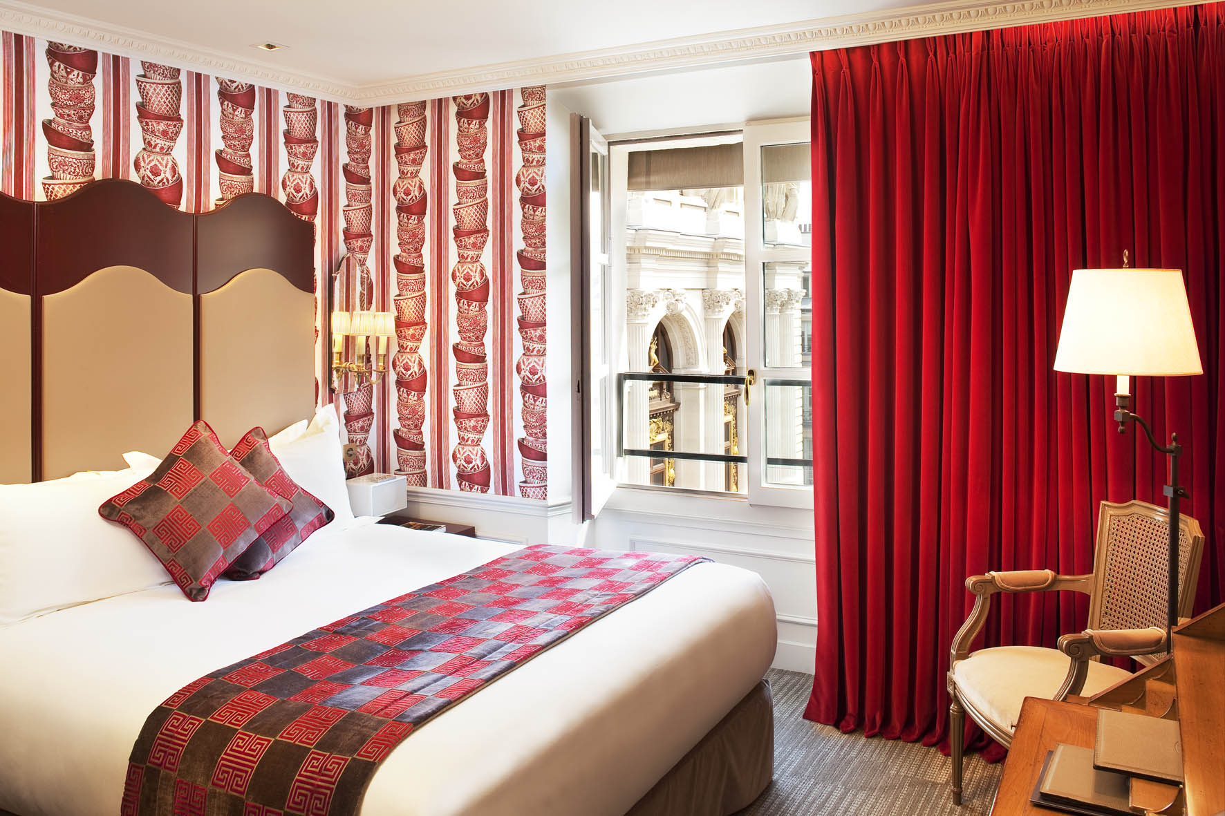 A room at La Maison Favart with red patterned wallpaper and red curtains
