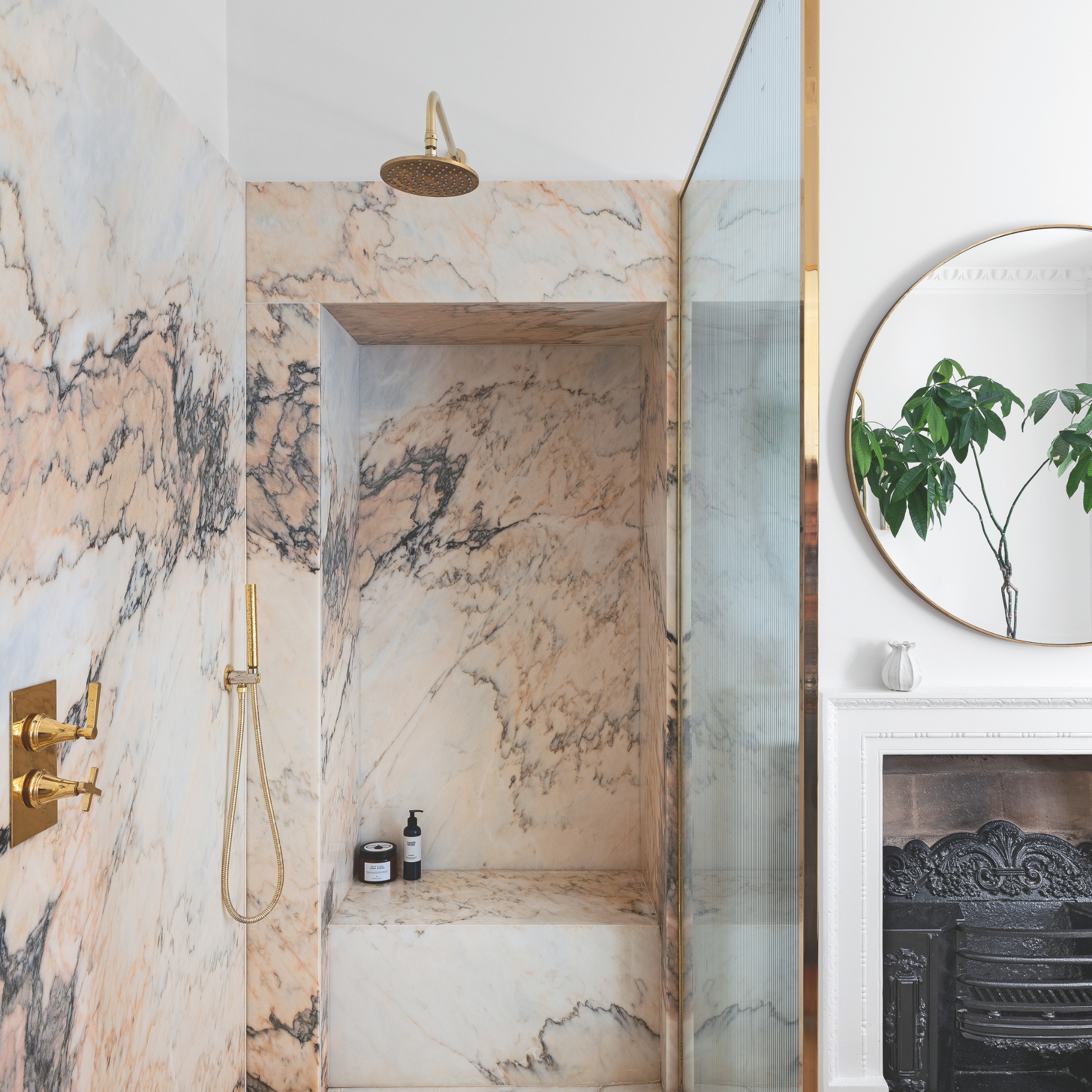 Pink marble tiles and gold accents in shower in a white bathroom.