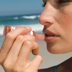 woman putting on lip balm on a beach