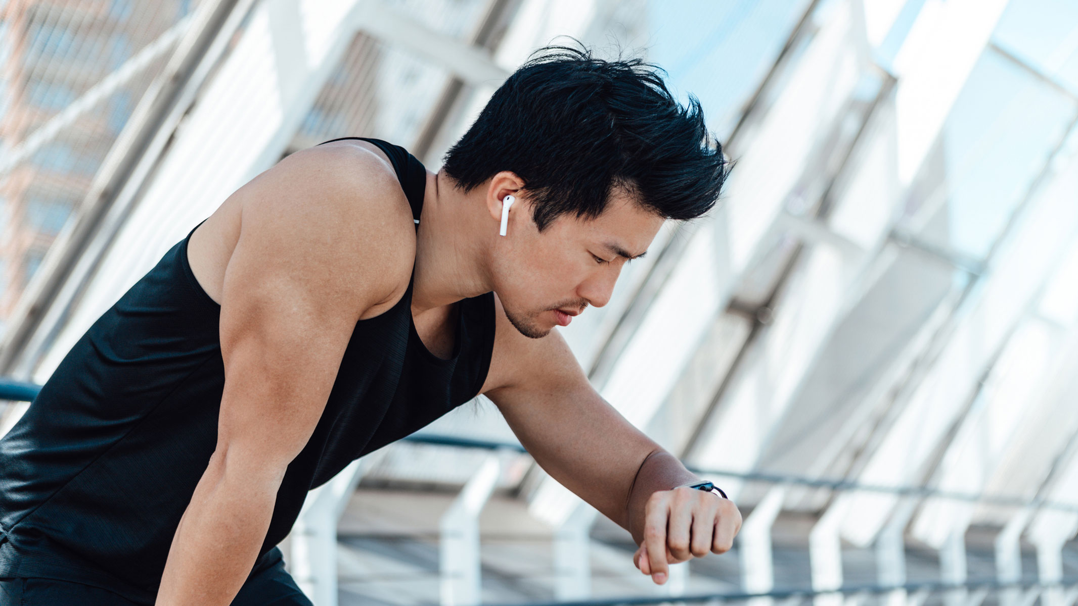 A picture of a young man looking at his smartwatch and listening to his earbuds