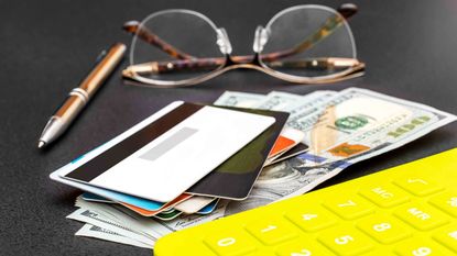 glasses with a yellow calculator and a stack of credit cards and money beside it