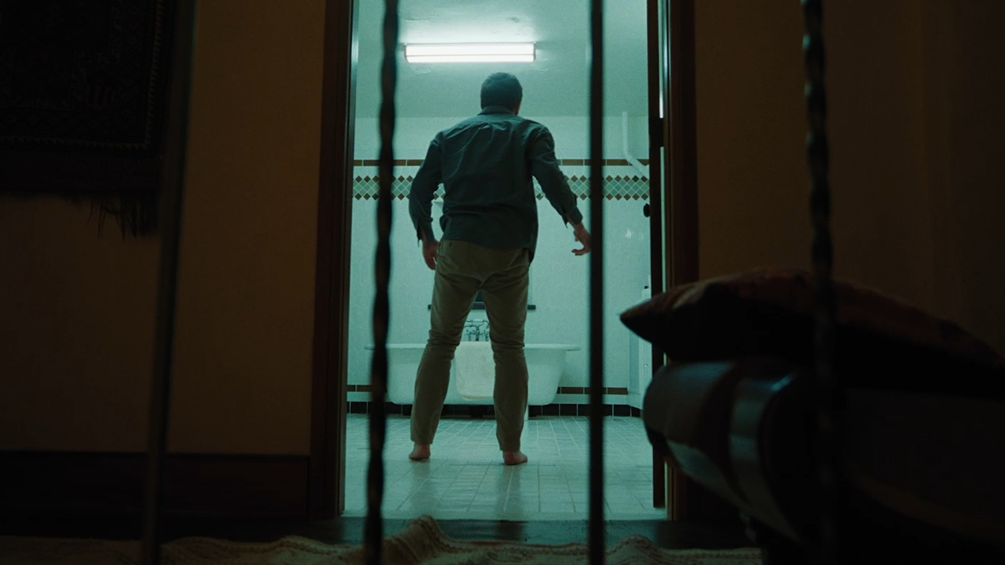 Jake Gyllenhaal standing in a bathroom, as seen through a doorway