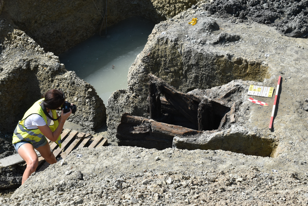An archaeological excavation of Celtic settlement; an archaeologist takes photos of the site with a camera.