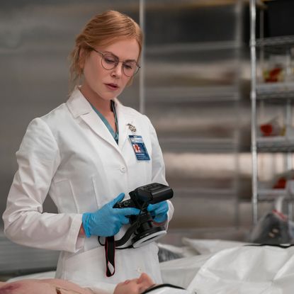 nicole kidman as kay scarpetta in a white labcoat and glasses examining a body in a still from prime video's scarpetta