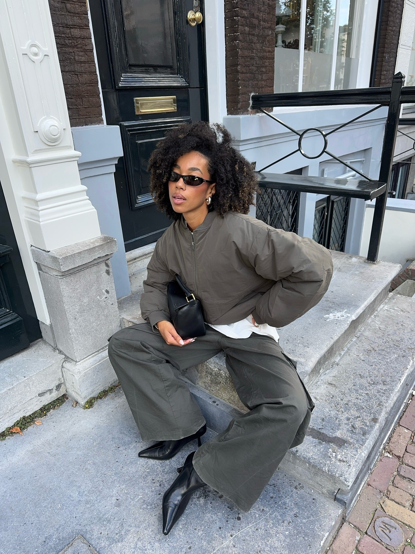 Influencer @amaka.hamelijnck wears a grey bomber jacket with khaki jeans and black pointed-toe kitten heels.
