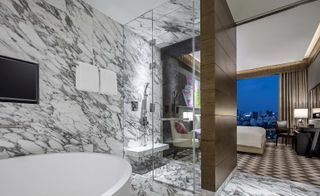 En-suite bathroom with white marble-effect tiles looking through into the bedroom