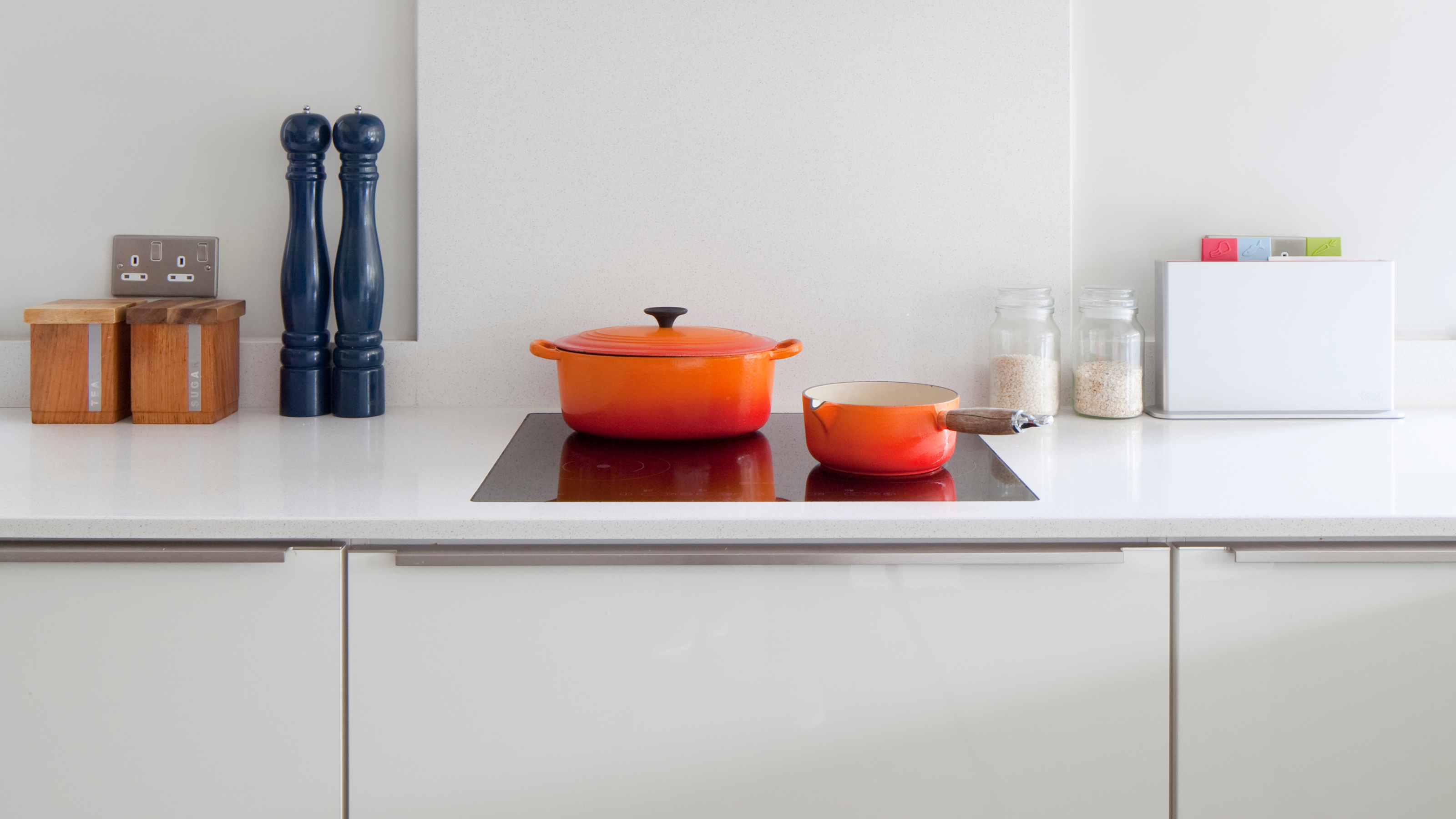 Two orange Le Creuset pans on a stove top in a modern white kitchen.
