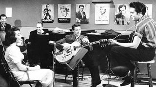 Elvis Presley performs on the set of his film 'Jailhouse Rock' with songwriter Mike Stoller (on piano), Scotty Moore (guitar), Judy Tyler, Bill Black and D.J. Fontana in 1957 in Hollywood, California