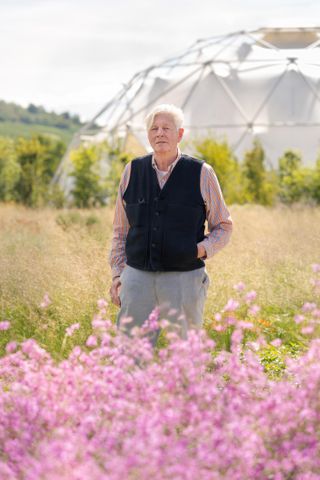 Dutch garden designer Piet Oudolf photographed among purple flowers in the garden he designed for Vitra in Weil am Rhein. Buckminster Fuller's dome is visible in the background